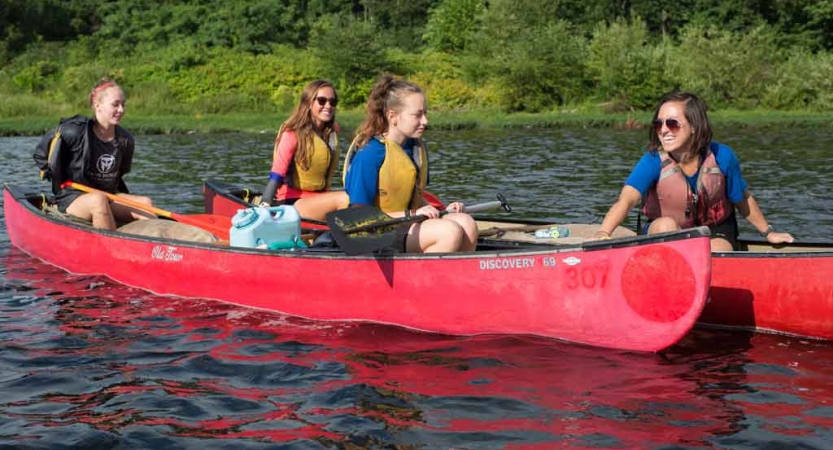 Two people each sit in two red canoes floating close together on calm water